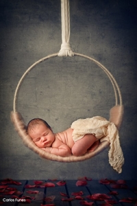 Fotografía de Marina. Una bebé preciosa que descansa sobre un aro colgado sobre un lecho de rosas. Fotografía por Carlos Funes. Especialista en retrato infantil y bebés.